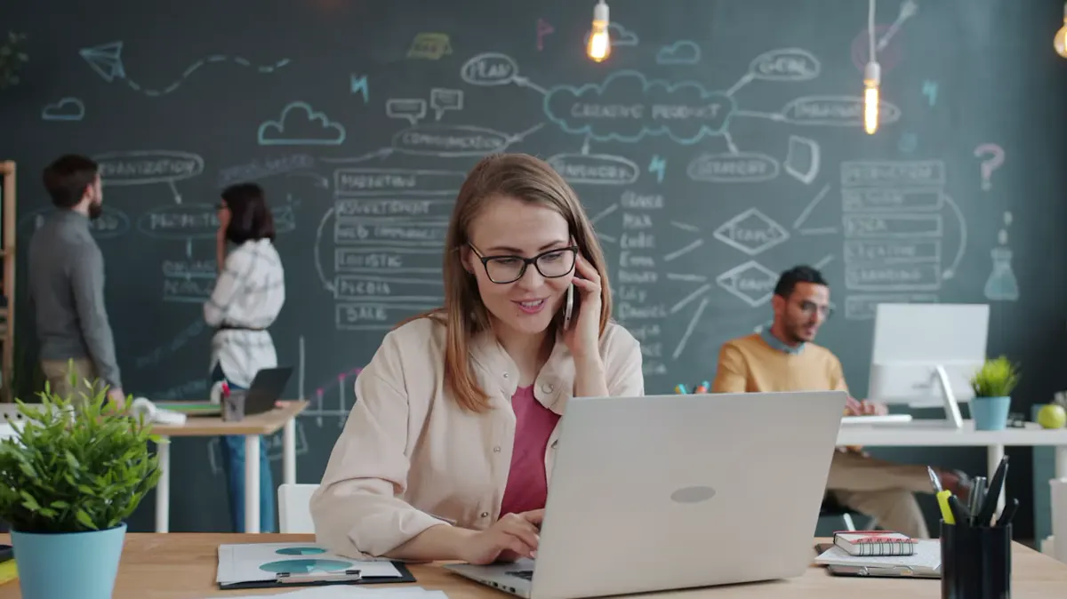 An office professional taking a call while working at a laptop.